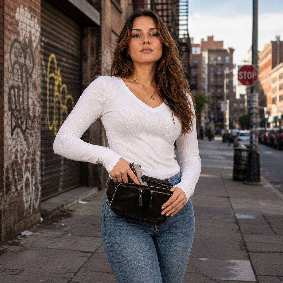 A woman wearing a white long-sleeve top and blue jeans stands on a city sidewalk, carrying a Unisex fanny pack Gun Leather Bag, Gun belt bag for men and women, Universal Holster Gun Bag, Concealed Carry Jessie Unisex Lambskin Belt Bag, DS Conceal, Outdoor Conceal Carry, best gun carrying sling, best gun carrying fanny pack