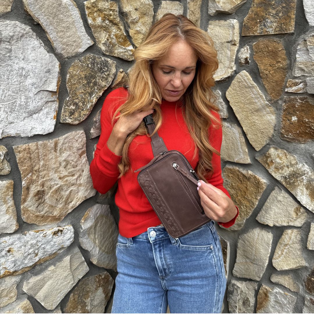 Woman holding a brown waist bag against a stone wall. Concealed Carry Kailey Leather Purse Pack - Lady Conceal - Concealed Carry Purse - most popular crossbody bag - crossbody handgun bag - crossbody bags for everyday use - Lady Conceal - Unique Hide Purse - Locking YKK Purse - Fanny Pack for Gun and Pistol - Easy CCW - Fast Draw Bag - Secure Gun Bag