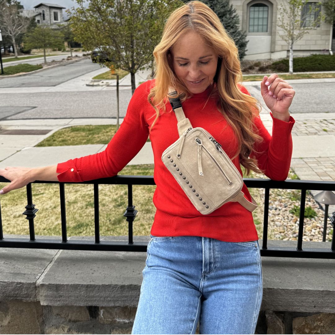 Woman in red sweater and blue jeans holding a beige crossbody bag on a balcony. Concealed Carry Kailey Leather Purse Pack - Lady Conceal - Concealed Carry Purse - most popular crossbody bag - crossbody handgun bag - crossbody bags for everyday use - Lady Conceal - Unique Hide Purse - Locking YKK Purse - Fanny Pack for Gun and Pistol - Easy CCW - Fast Draw Bag - Secure Gun Bag